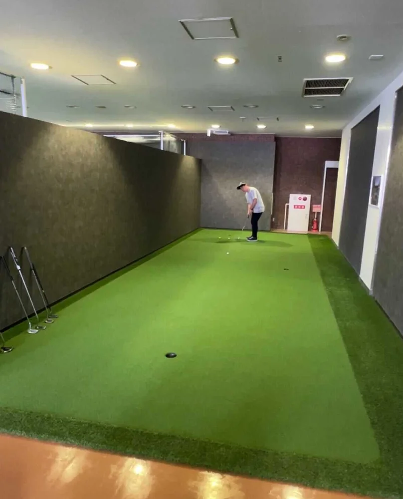 商業施設内に設置された、壁面と人工芝のパターゴルフ練習スペースでパッティングをする人