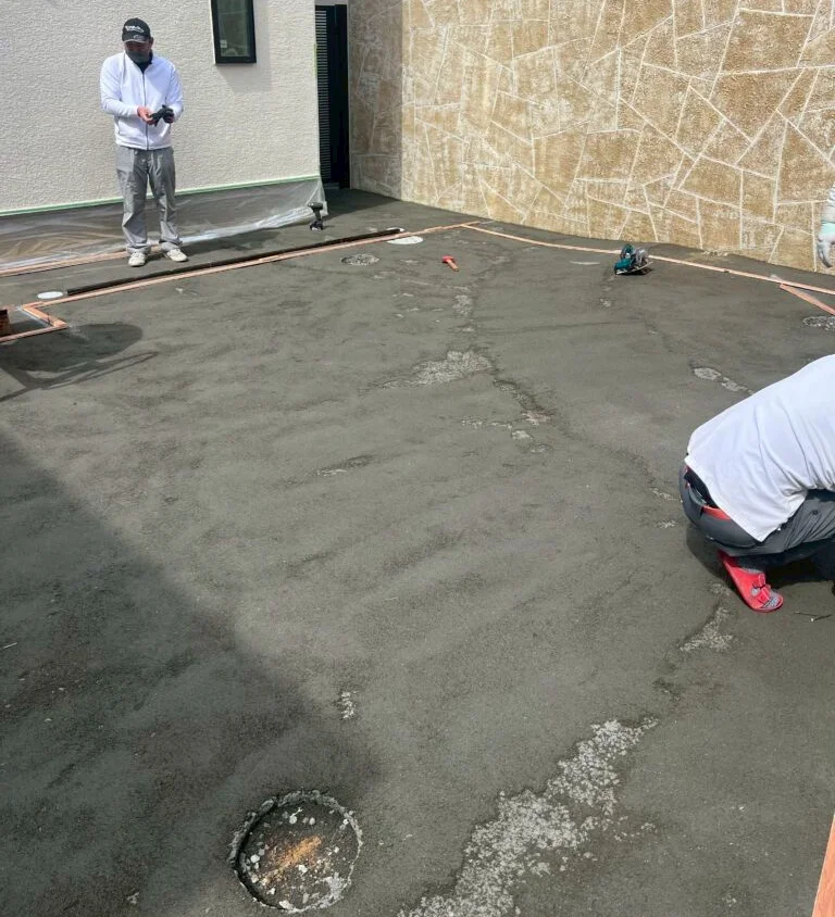 パターグリーン施工前の、コンクリート下地を左官仕上げした戸建て住宅の庭と作業スタッフ