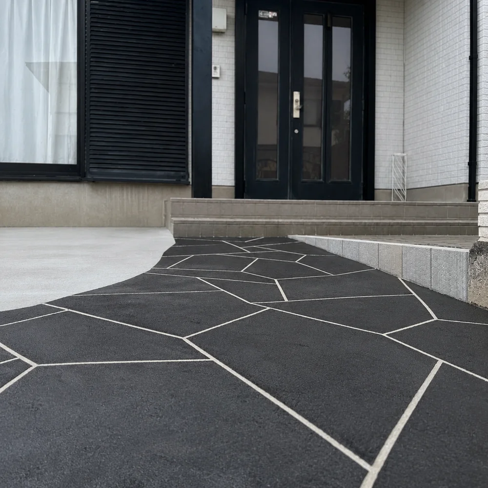 白い外壁と黒い玄関ドアの住宅前に施工した、黒い石材風のTFフロアの玄関アプローチ